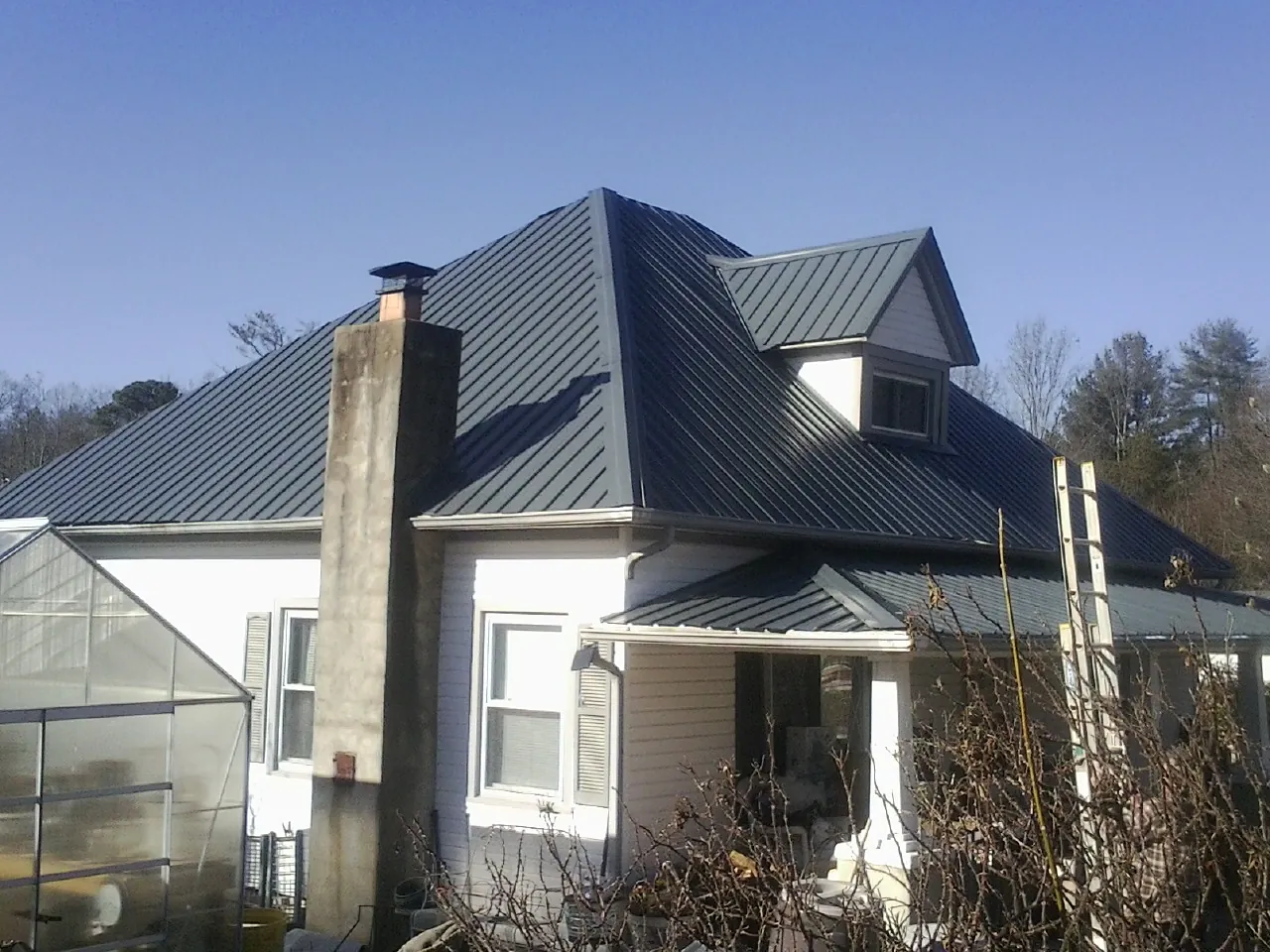 Dark blue standing seam metal roof on a white farmhouse with dormer — Slate & Tile Roof Repair by Roofing Brothers in White Lake